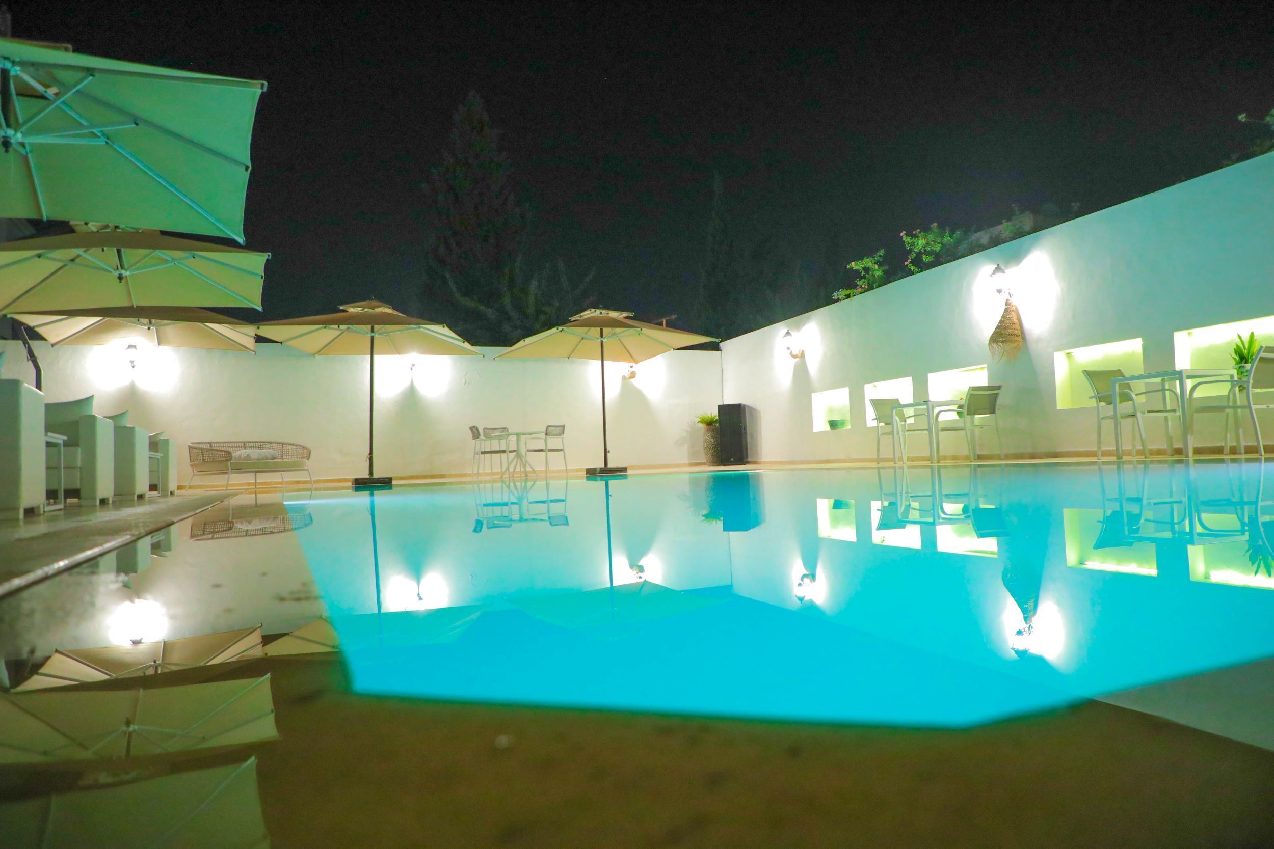 Uma área de piscina à noite, com vários guarda-sóis e espreguiçadeiras.