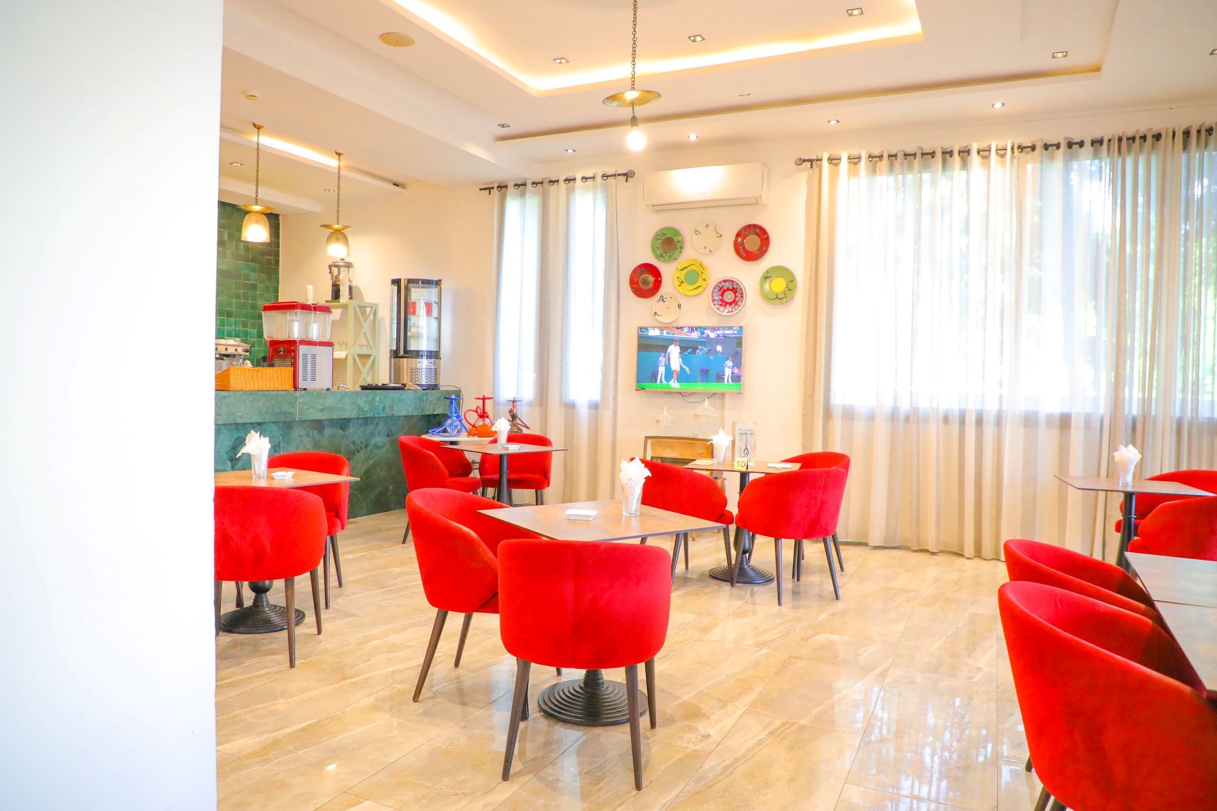 Een modern restaurant met rode stoelen en tafels, een toonbank met een kassa en een televisie aan de muur.