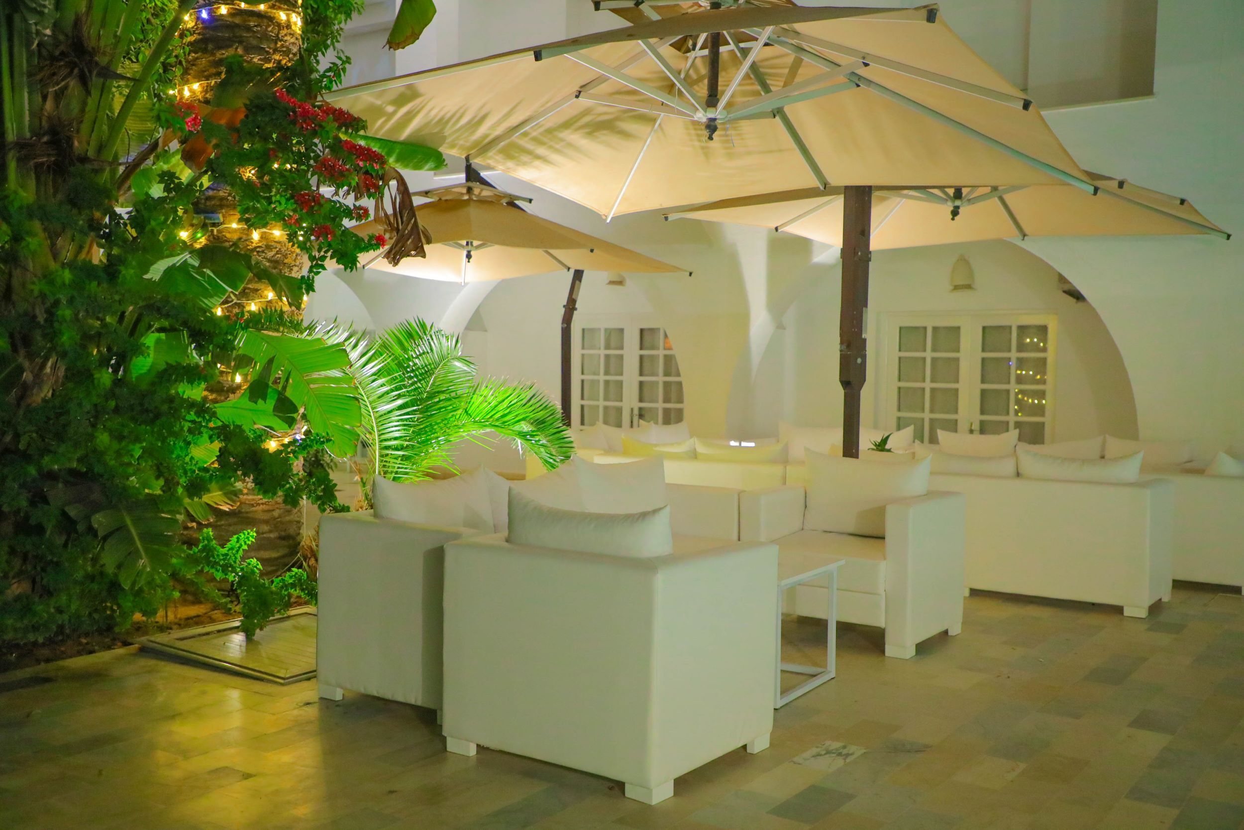 Een moderne, overdekte lounge met witte banken en een grote parasol.