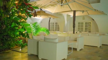 Een moderne, overdekte lounge met witte banken en een grote parasol.