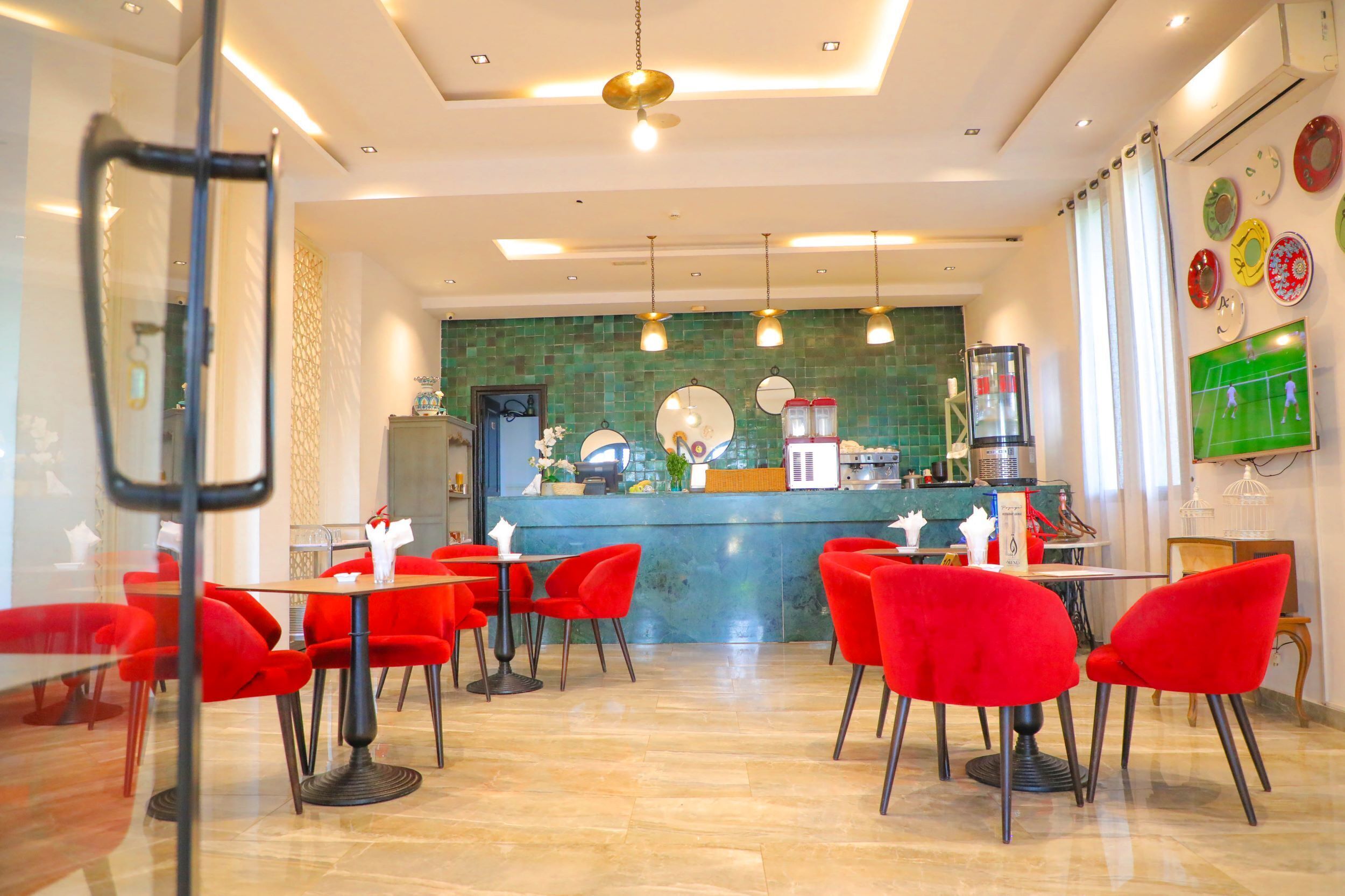 Un restaurant avec des chaises et des tables rouges, un comptoir orné d’un décor en mosaïque verte et une décoration murale sur le thème du sport.