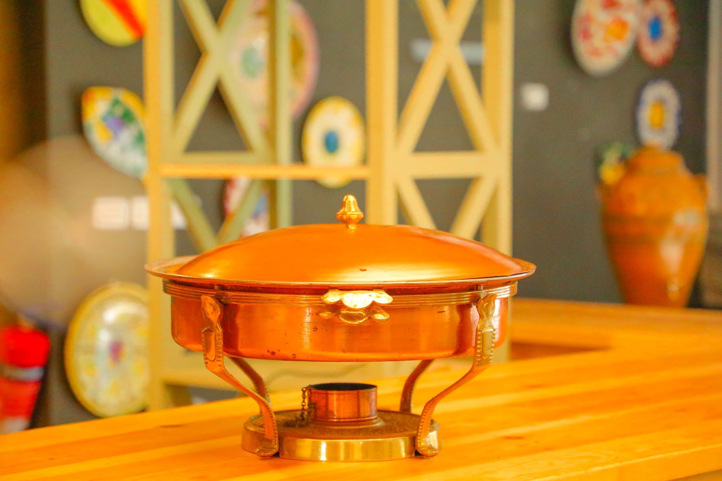 A brass stove with a lid on a wooden table.