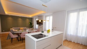 A modern kitchen with a central island, dining area with a sofa and chairs, and a TV mounted on the wall.
