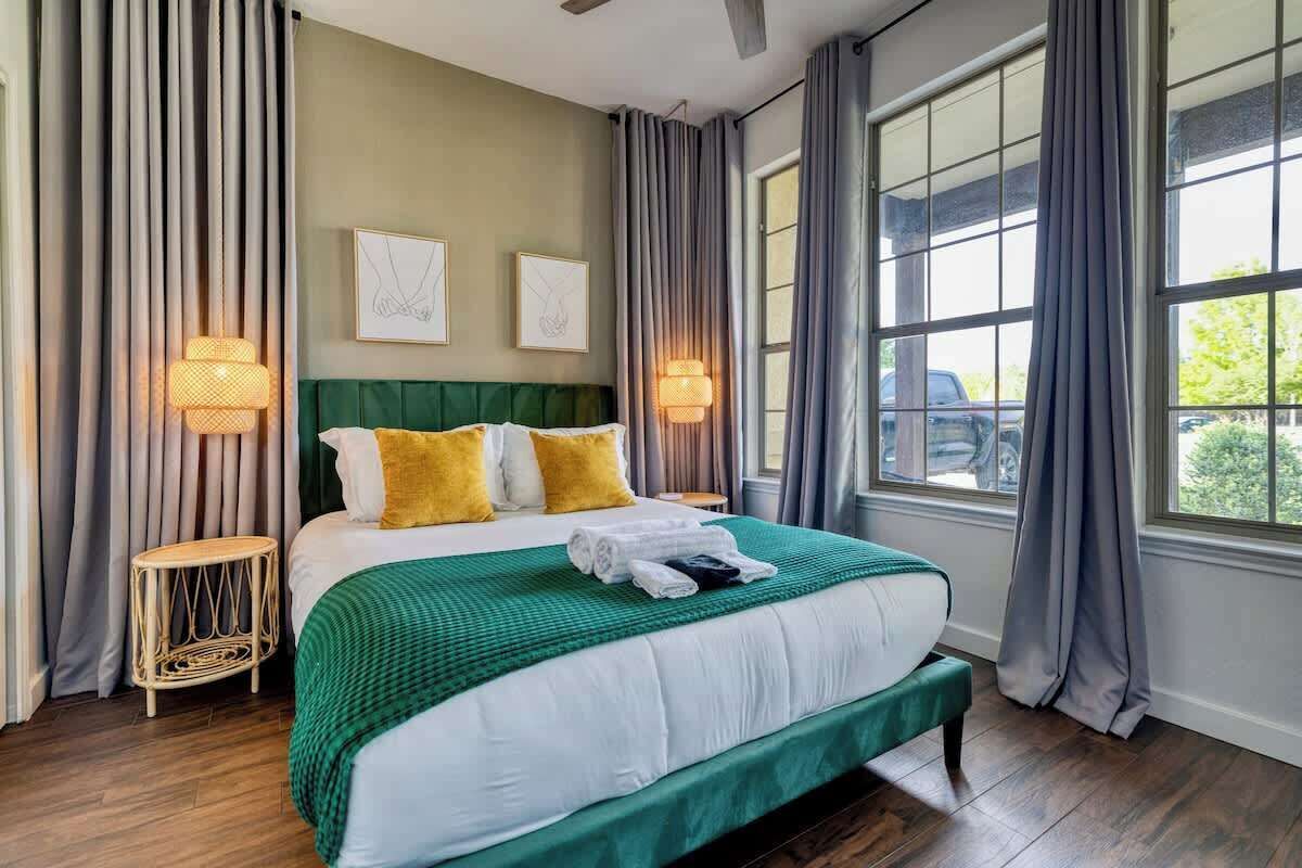 A neatly made bed with a green bedspread, two pillows, and a bedside lamp.
