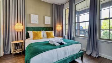 A neatly made bed with a green bedspread, two pillows, and a bedside lamp.