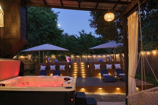 An outdoor hot tub area with a wooden deck, lounge chairs, and ambient lighting.