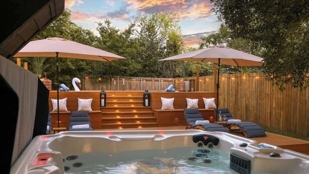A hot tub with lounge chairs and umbrellas, surrounded by a wooden deck and a wooden fence. - 6 Bedroom Villa | Pool | Hot Tub Cabana (Austin)
