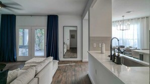 A modern living room with a sofa, a dining area with a kitchen counter, and a hallway leading to another room. - 6 Bedroom Villa | Pool | Hot Tub Cabana (Austin)