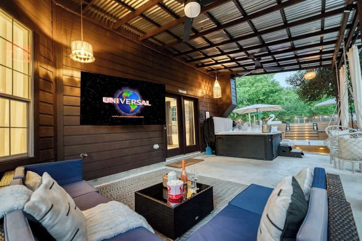A cozy outdoor seating area with a flat-screen TV displaying 'UNIVERSAL,' a wooden exterior, and a well-lit patio with outdoor furniture.
