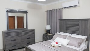 Ein Schlafzimmer mit Bett, Kommode, Nachttisch, Spiegel und Klimaanlage.