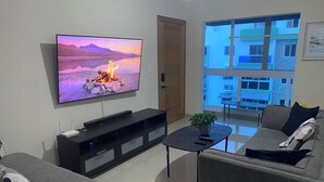 Ein Wohnzimmer mit Flachbildfernseher, einer schwarzen Unterhaltungsanlage, einem grauen Sofa, einem kleinen Couchtisch mit Pflanze und einem Fenster mit Blick auf Gebäude.