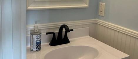 A bathroom with a white sink, black faucet, and a mirror above it. There is a bottle of hand soap on the sink counter.