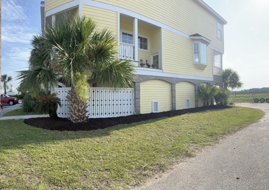 A two-story house with a balcony, a fenced yard, and a palm tree.