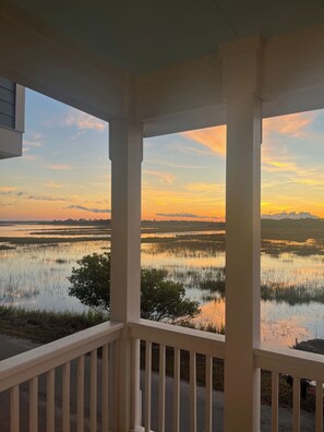 Vista de um alpendre coberto para um corpo de água calma com o pôr do sol ao fundo.