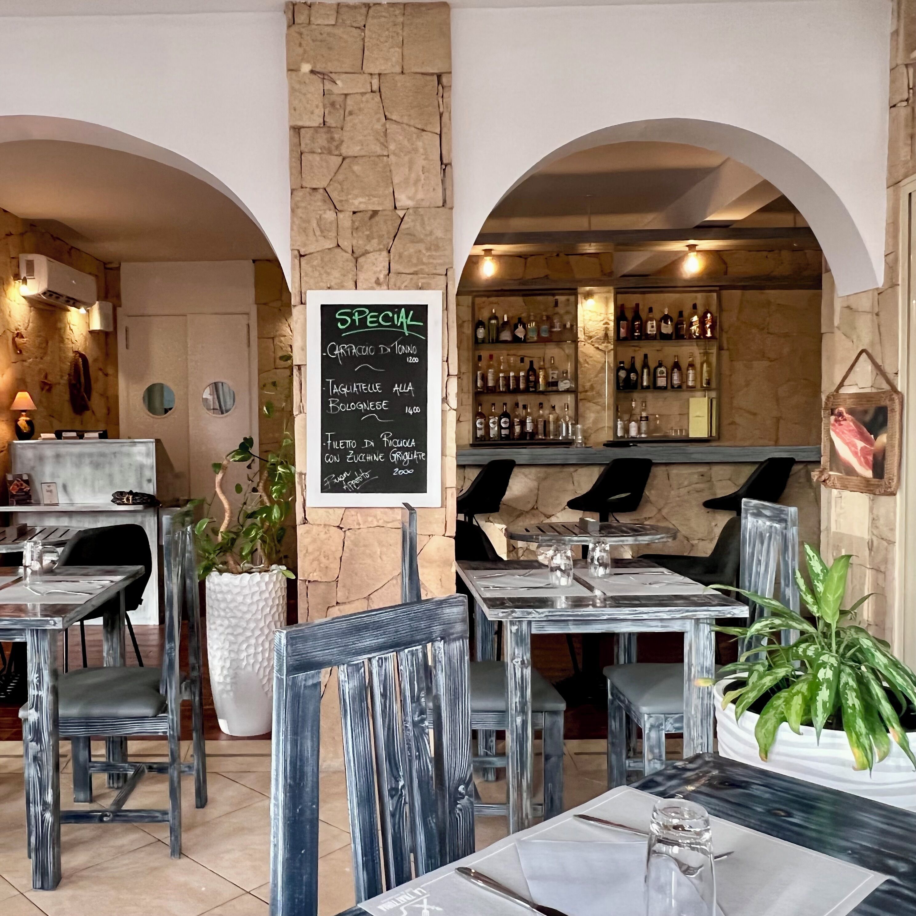 A restaurant interior with stone walls, a chalkboard menu, and a bar area.