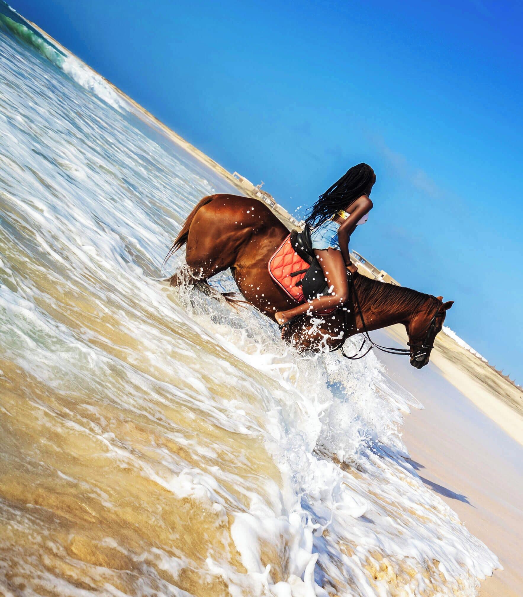 Eine Person reitet auf einem Pferd an einem Strand, während Wellen an das Ufer schlagen.