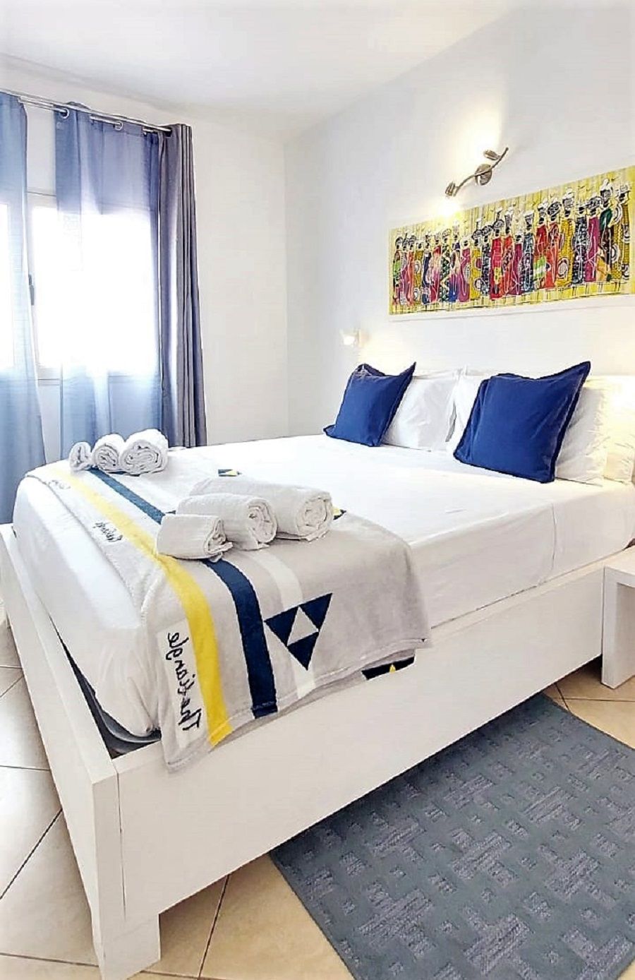 A hotel room with a bed, pillows, a blanket, and a wall art piece.