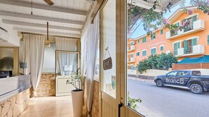 A hotel reception area with a tiled floor, a reception desk, a large potted plant, and a view of a parked truck outside. - Branco Suites (Sal)