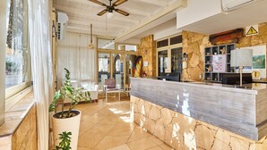 A reception area with a stone wall, a reception desk, and a ceiling fan. - Branco Suites (Sal)