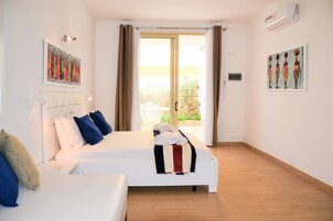 Habitación de hotel con cama, sofá y puerta corrediza de vidrio que da a un área exterior.