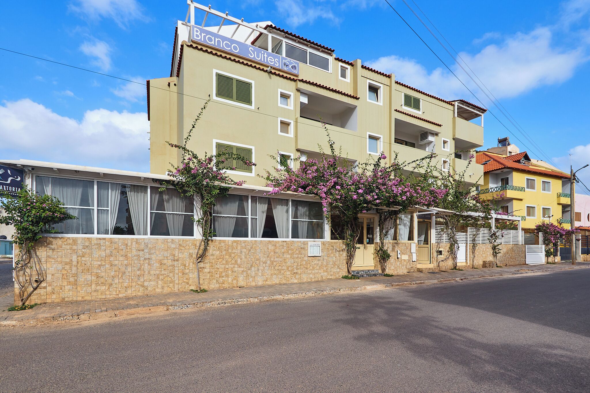 A hotel named "Branco Suites" with a tiled facade, multiple balconies, and a clear sky.