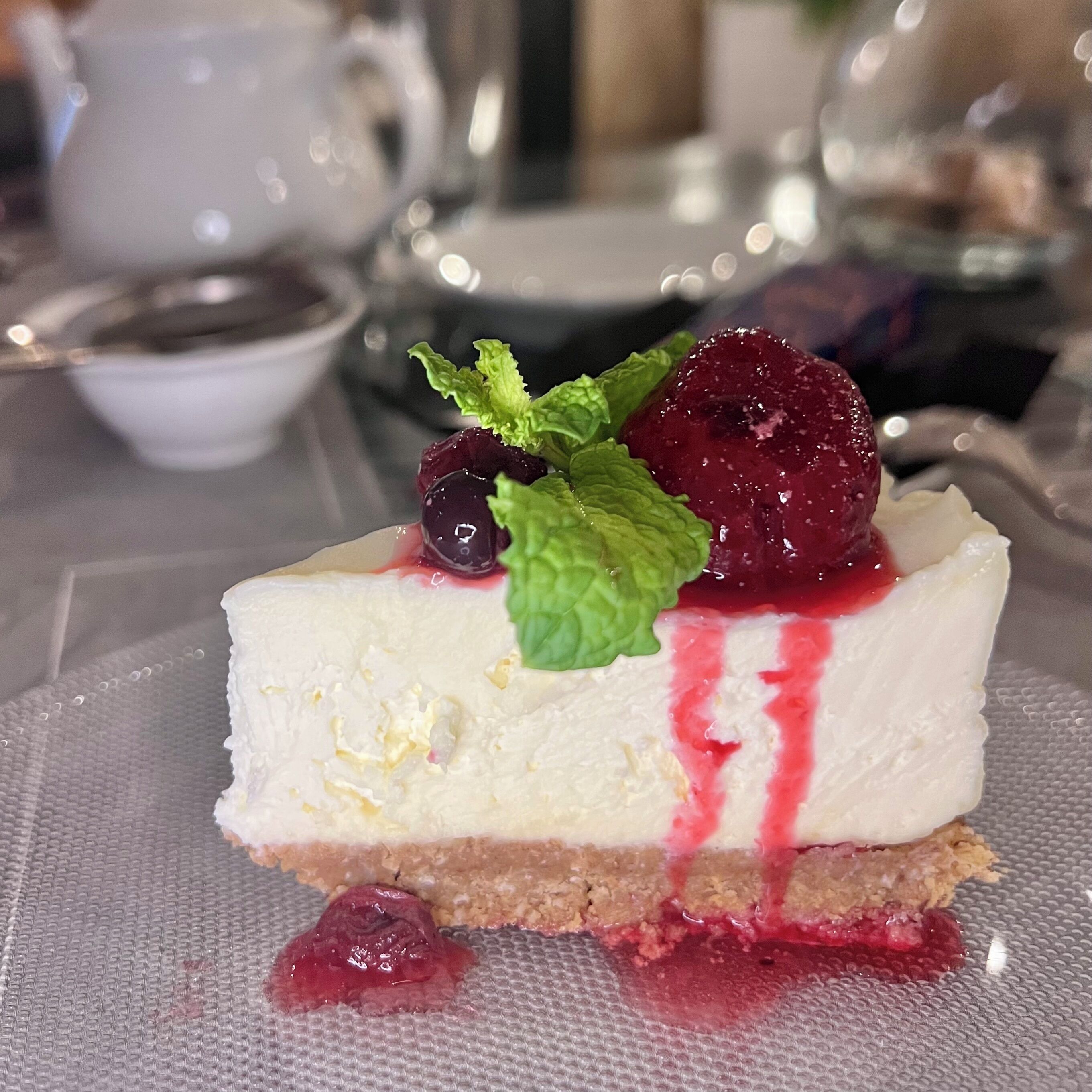 A slice of cheesecake with berries and mint on a plate.