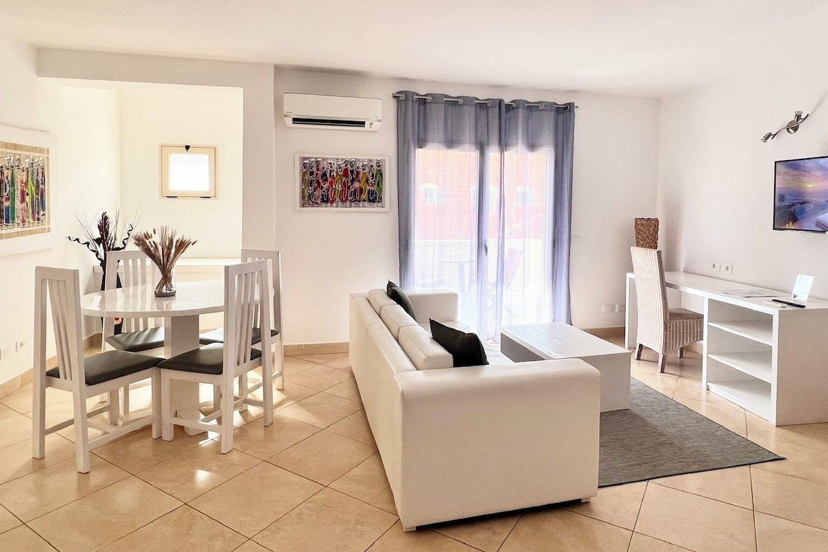 Uma sala de estar moderna com um sofá branco, mesa de jantar, cadeiras e uma televisão.