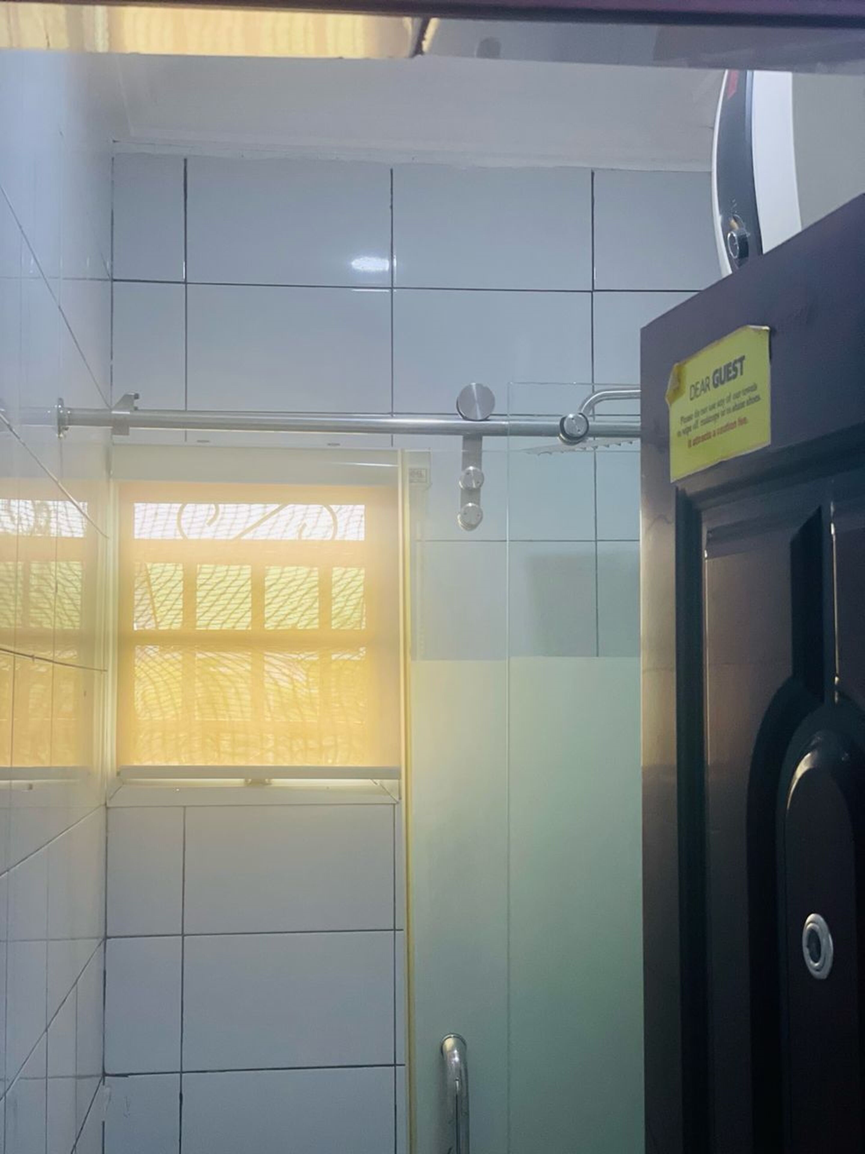 A restroom with a handrail, a sign that reads "DEAR GUEST," and a window with a metal grid.