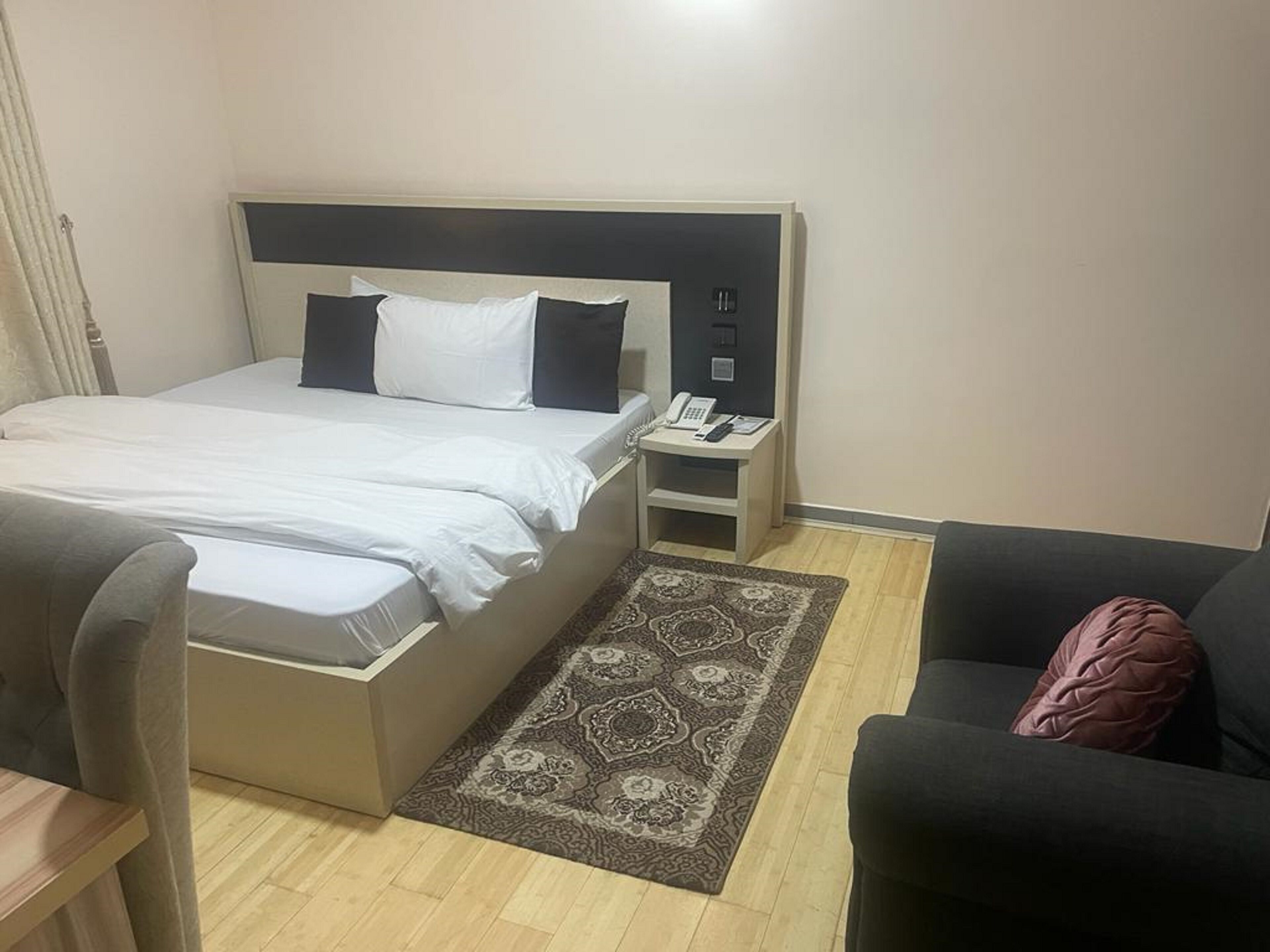 Una habitación de hotel con cama, mesita de noche con teléfono, una silla y un sofá.