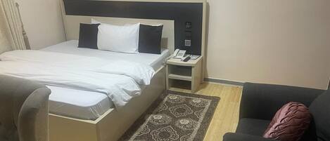 Una habitación de hotel con cama, mesita de noche con teléfono, una silla y un sofá.