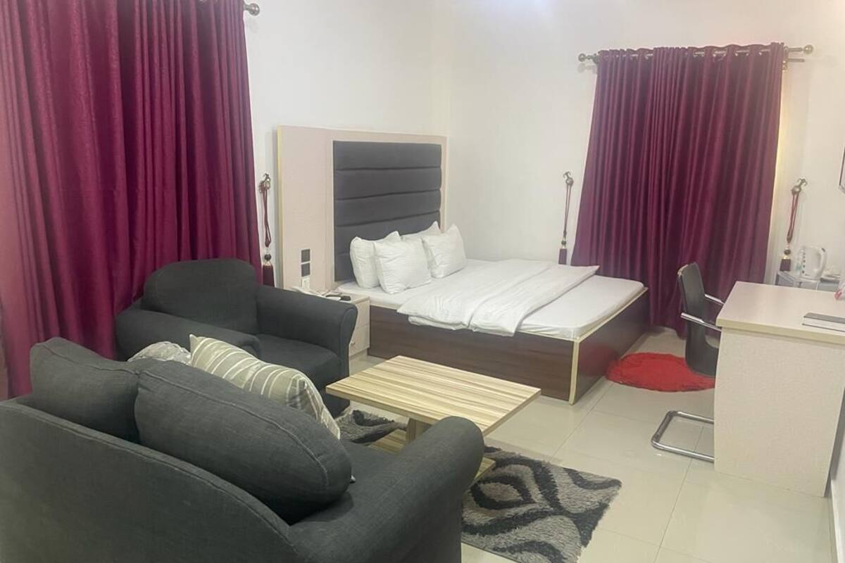 A compact hotel room with a bed, a sofa, a small desk, and a chair.