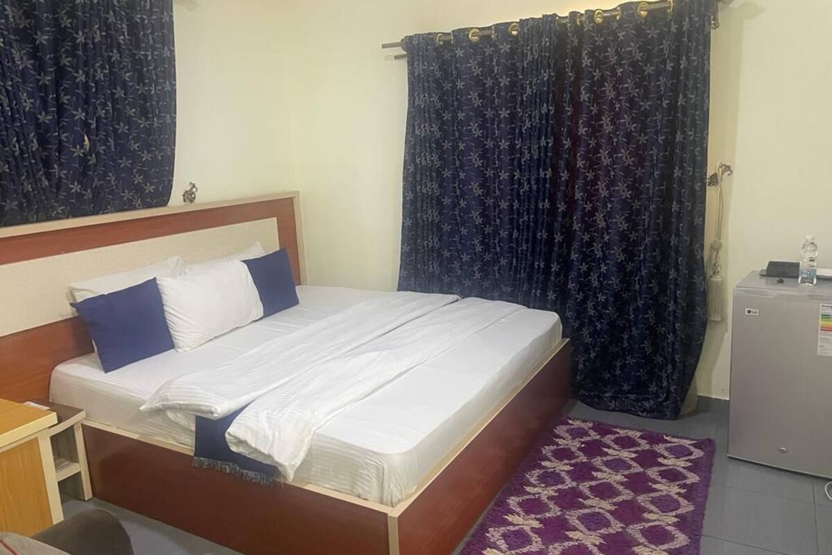 A neatly made bed with white and blue bedding, a wooden headboard, and a purple patterned rug on the floor.