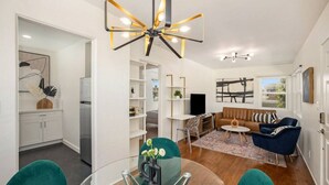 Een moderne woonkamer met een glazen eettafel, teal stoelen, een bruine bank en een bijzondere plafondlamp.