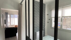 A modern bedroom with a large window, a bed with a light-colored duvet, and a black wardrobe. - L'escale, Appartement au Cœur de Granville (Granville)