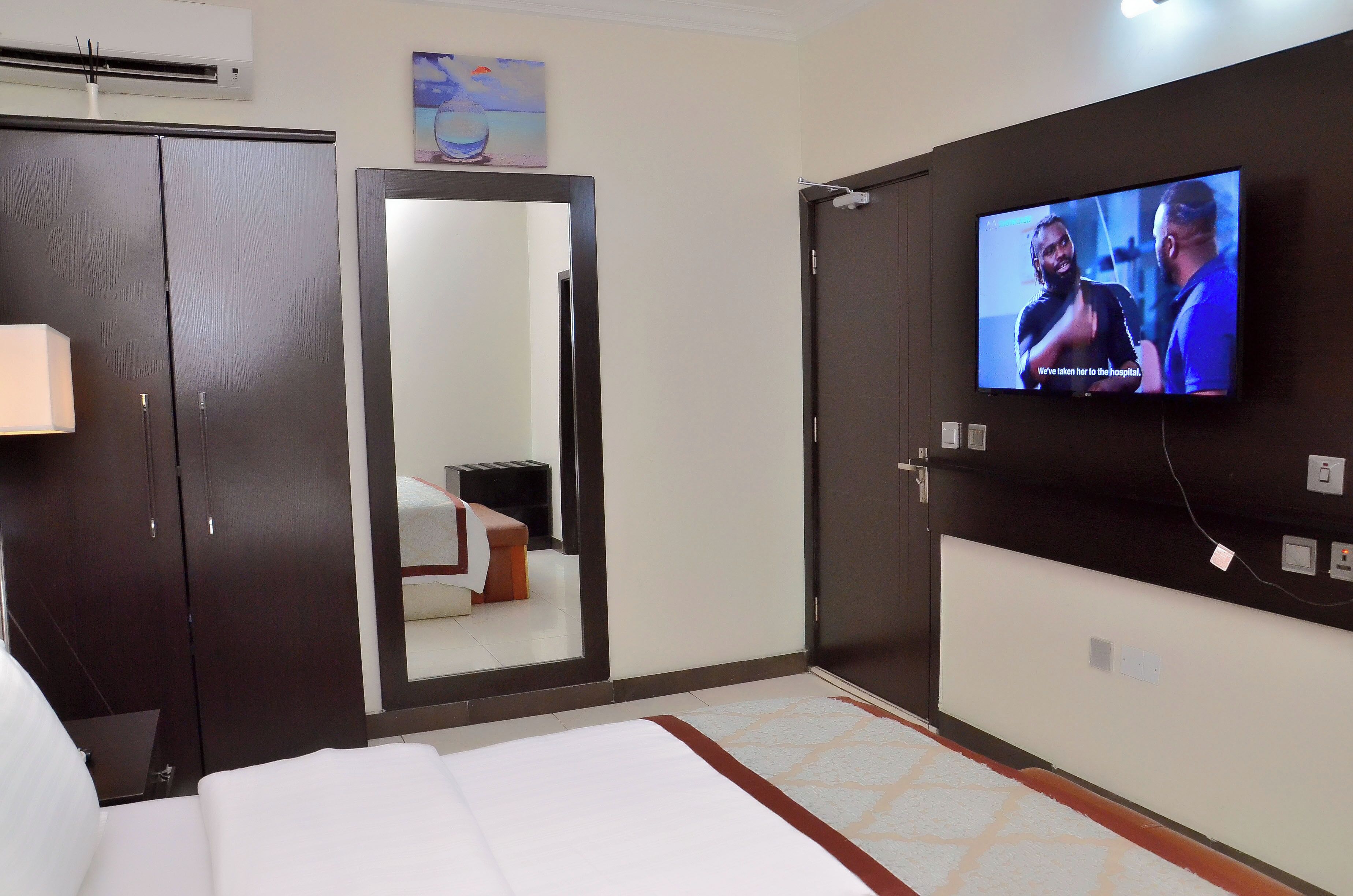 A hotel room with a bed, a TV mounted on the wall, a wardrobe, and a mirror.