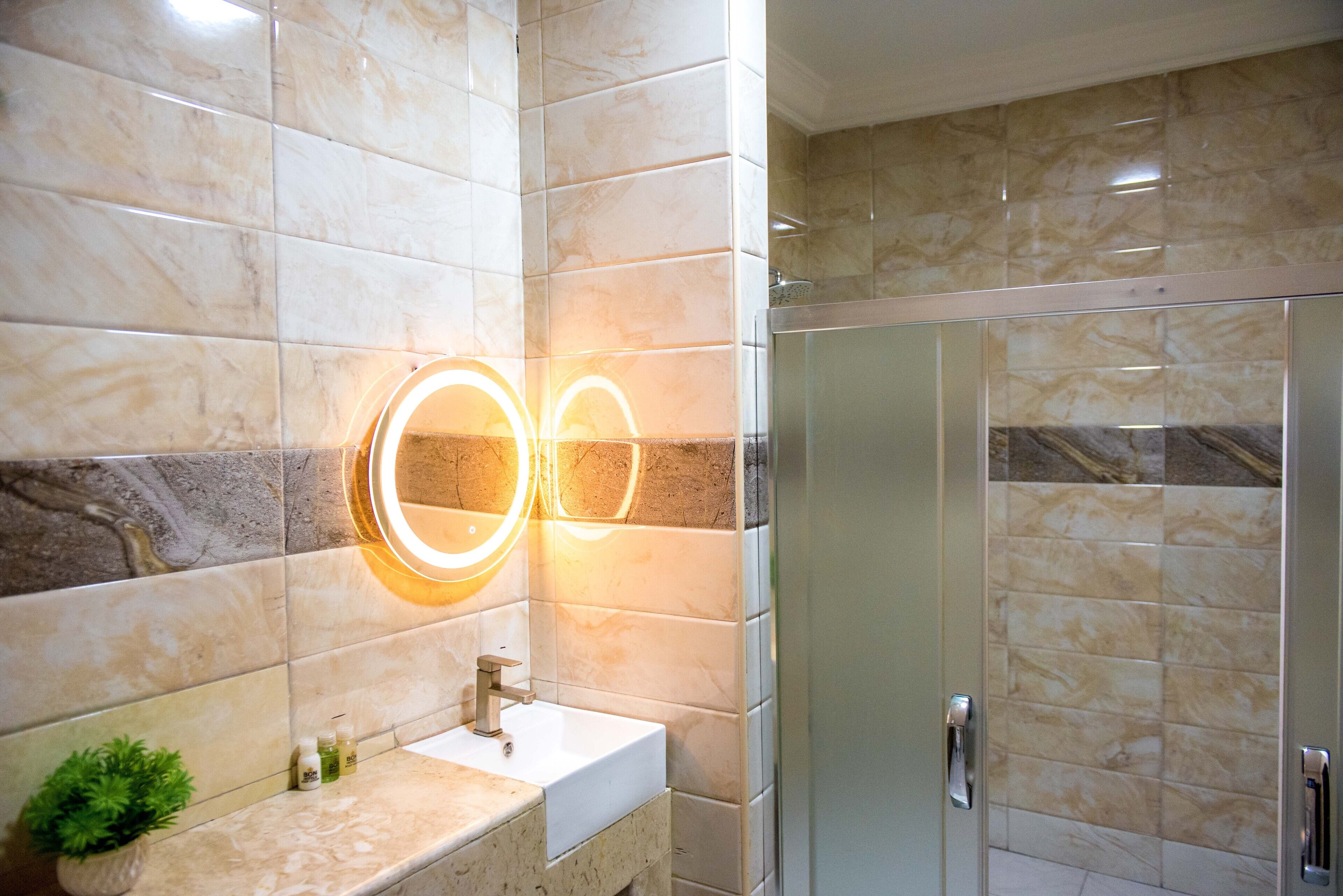 A bathroom with a marble sink, a mirror with illuminated lights, and a glass shower enclosure.