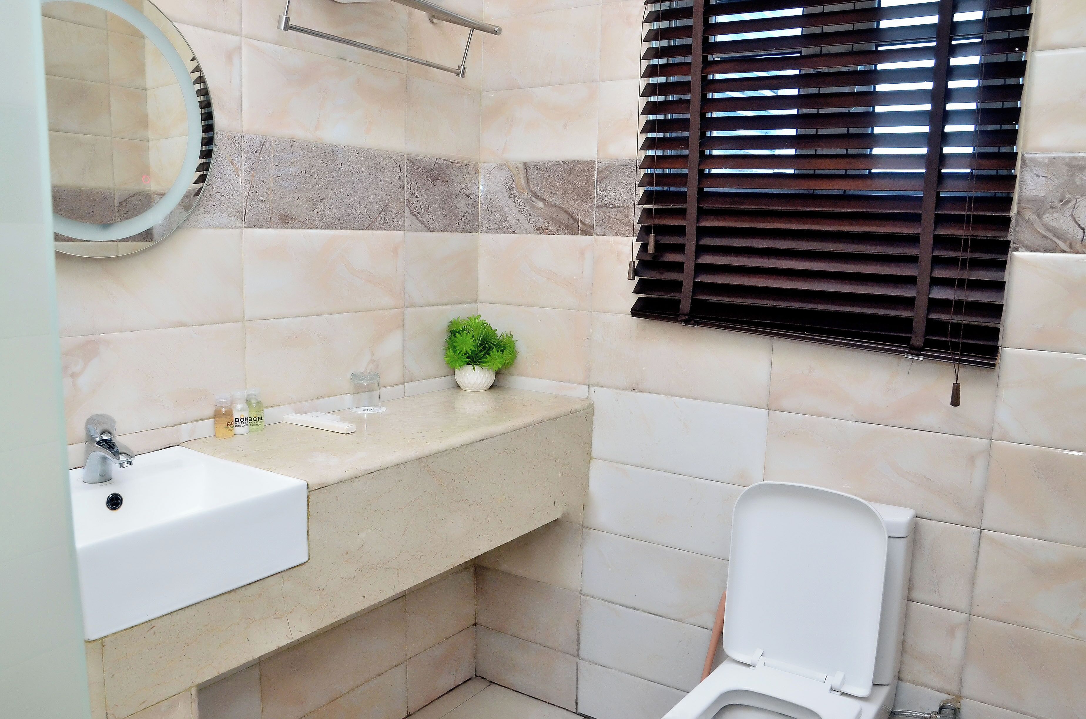 A bathroom with a white sink, a mirror, a toilet, and a window with blinds.