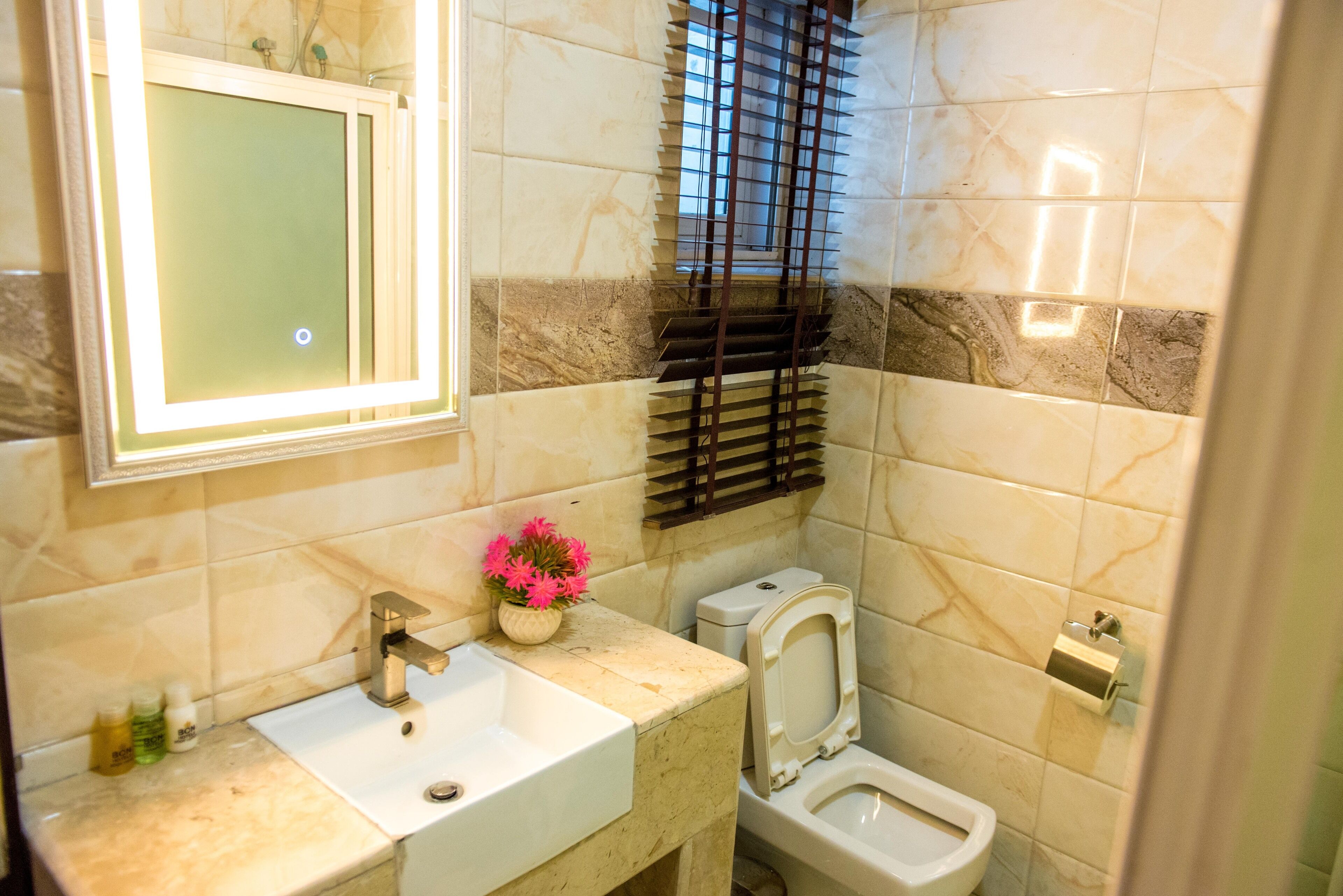 Un baño con lavamanos, espejo, inodoro y una ventana con persianas.