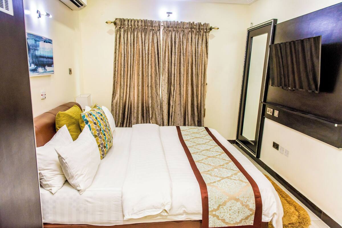 Une chambre d’hôtel avec un lit, une télévision, un miroir et des rideaux.
