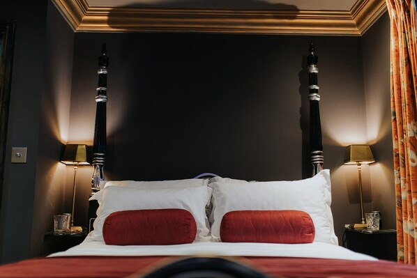Una habitación de hotel con una cama con dosel, dos lámparas de noche y un cabecero oscuro.