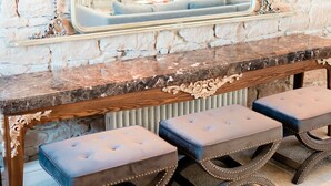A stone wall with a mirror above a wooden console table with three cushioned stools. - Newton Hall Courtyard Rooms (Alnwick)