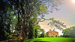 A large, historic building with a symmetrical facade, surrounded by a well-maintained lawn and mature trees. - Newton Hall Courtyard Rooms (Alnwick)