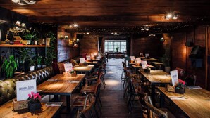 A restaurant with wooden tables and chairs, a leather booth, and potted plants. - Newton Hall Courtyard Rooms (Alnwick)