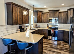 A modern kitchen with dark wooden cabinets, a stainless steel refrigerator, a built-in microwave, and a large island with bar stools. - 5th Street Retreat, quiet townhome a short walk from the heart of Loveland (Loveland)