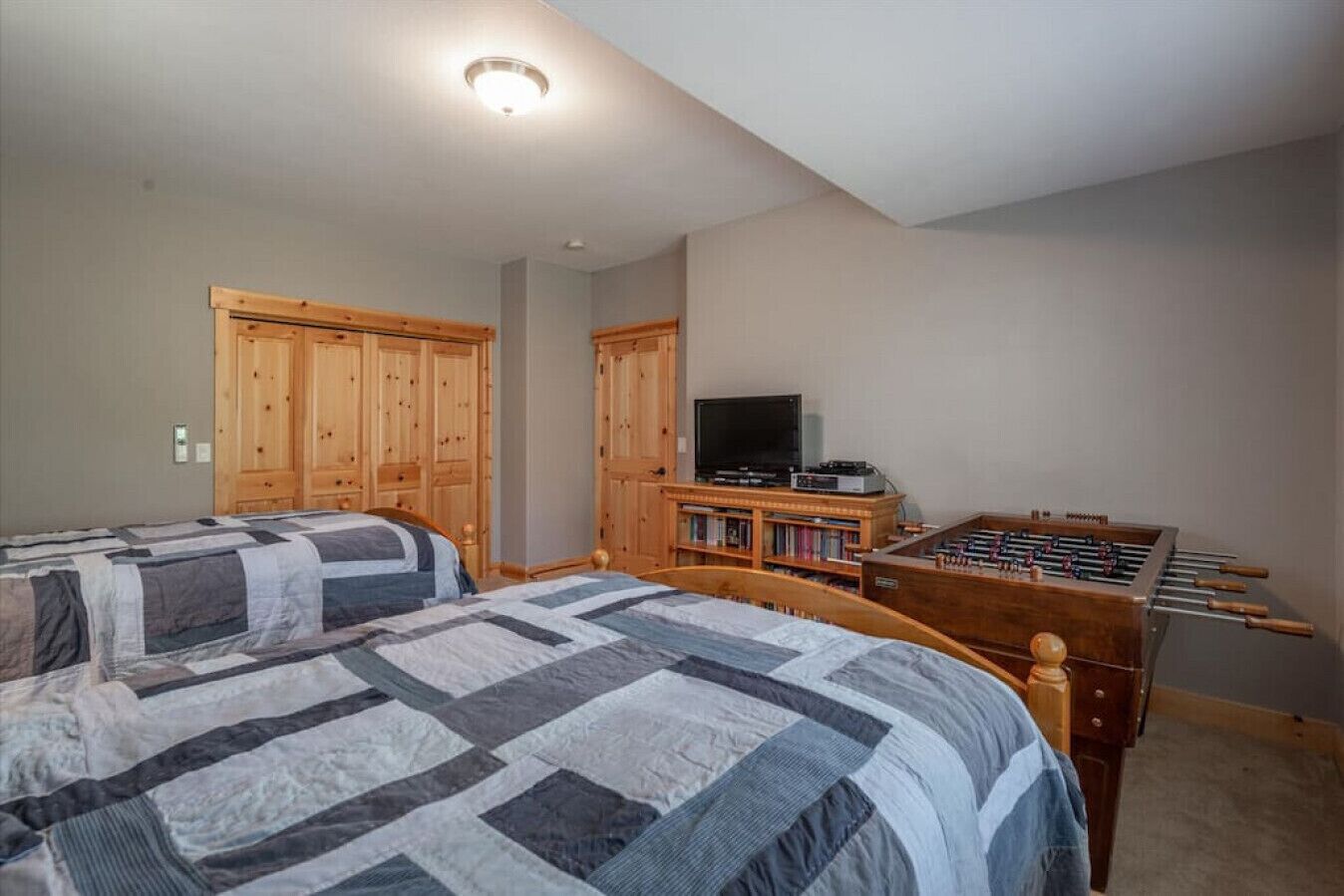 Un dormitorio con dos camas, un armario de madera, un televisor y una mesa de fútbol.