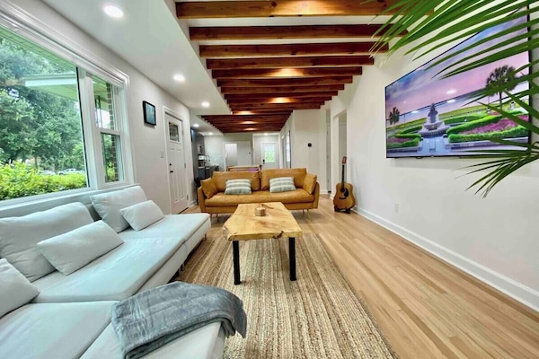 Step into the spacious living room with a vibrant Majesty Palm, where the eye is drawn upward to the striking exposed ceiling beams, creating a harmonious blend of nature and architectural charm.