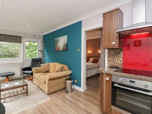 A modern kitchen with a red range hood, a dining area with a leather chair, and a cozy living room with a beige sofa. - The Lodge (Ambleside)