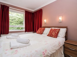 A neatly made bed with floral bedding, red curtains, and two bedside lamps.