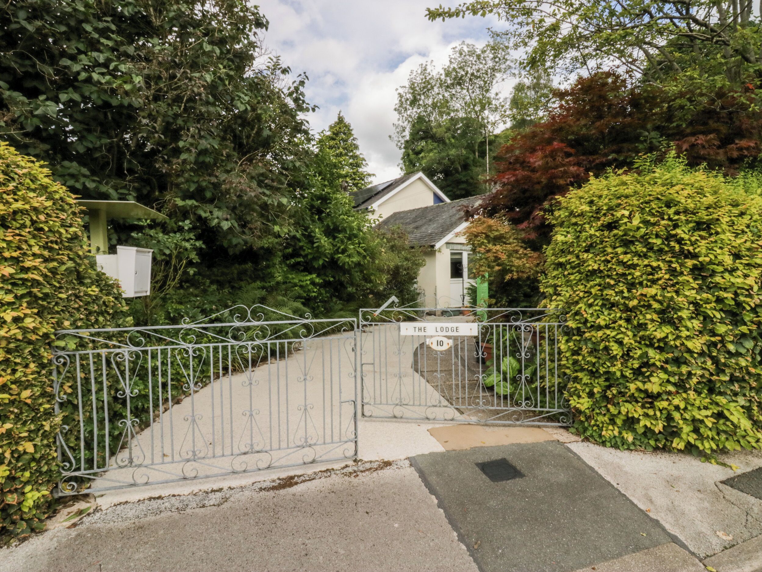Une entrée fermée par un portail donnant accès à une propriété appelée « The Lodge », avec un portail en métal et une allée pavée menant à une maison.