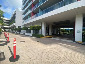 A modern building with multiple floors, a covered entrance, and a paved walkway with bollards. - Beautiful 2-Queen Bed Apt w/Pool & Beach Service (Hallandale Beach)